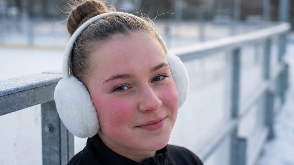 Young woman in white earmuffs, low bun, at ice rink.