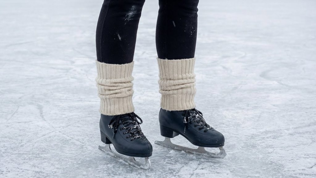 Person in black leggings and beige leg warmers ice skating on a frozen rink.