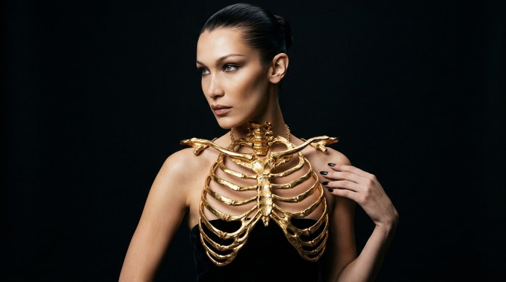 Person in black outfit wearing a gold ribcage-style chest piece and necklace against a dark background