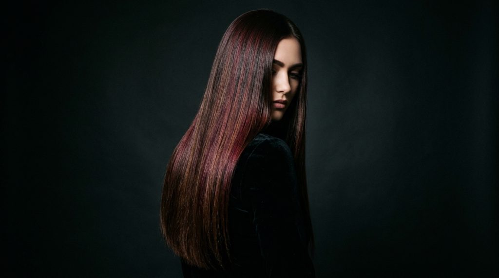 Person in profile with long straight auburn hair against a dark studio background