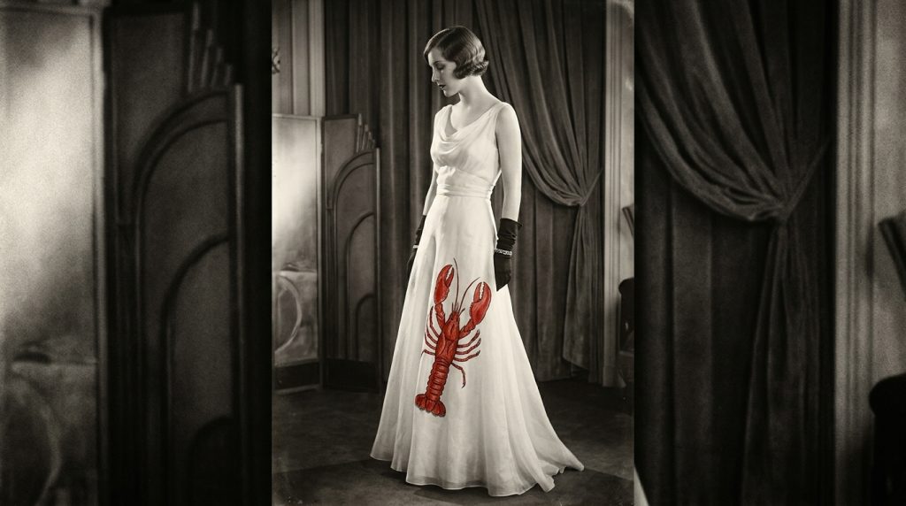 Vintage black-and-white photo of a woman in a white gown with a red lobster design, posing by curtains.