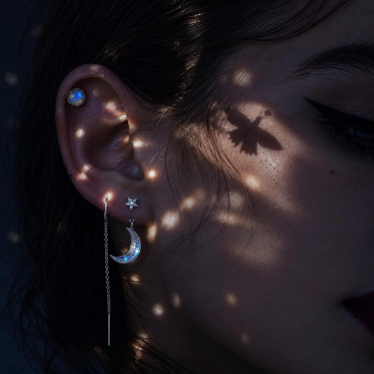 Close-up of ear with star and crescent moon earrings, shimmering light spots, and a bird shadow on cheek