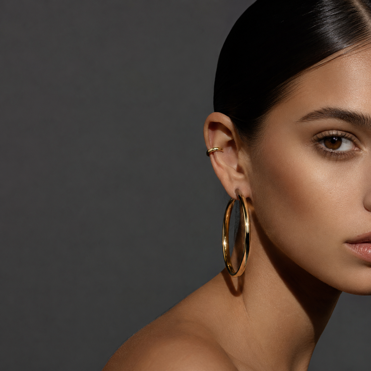 Close-up portrait of woman with sleek dark hair wearing large gold hoop earrings against a dark background