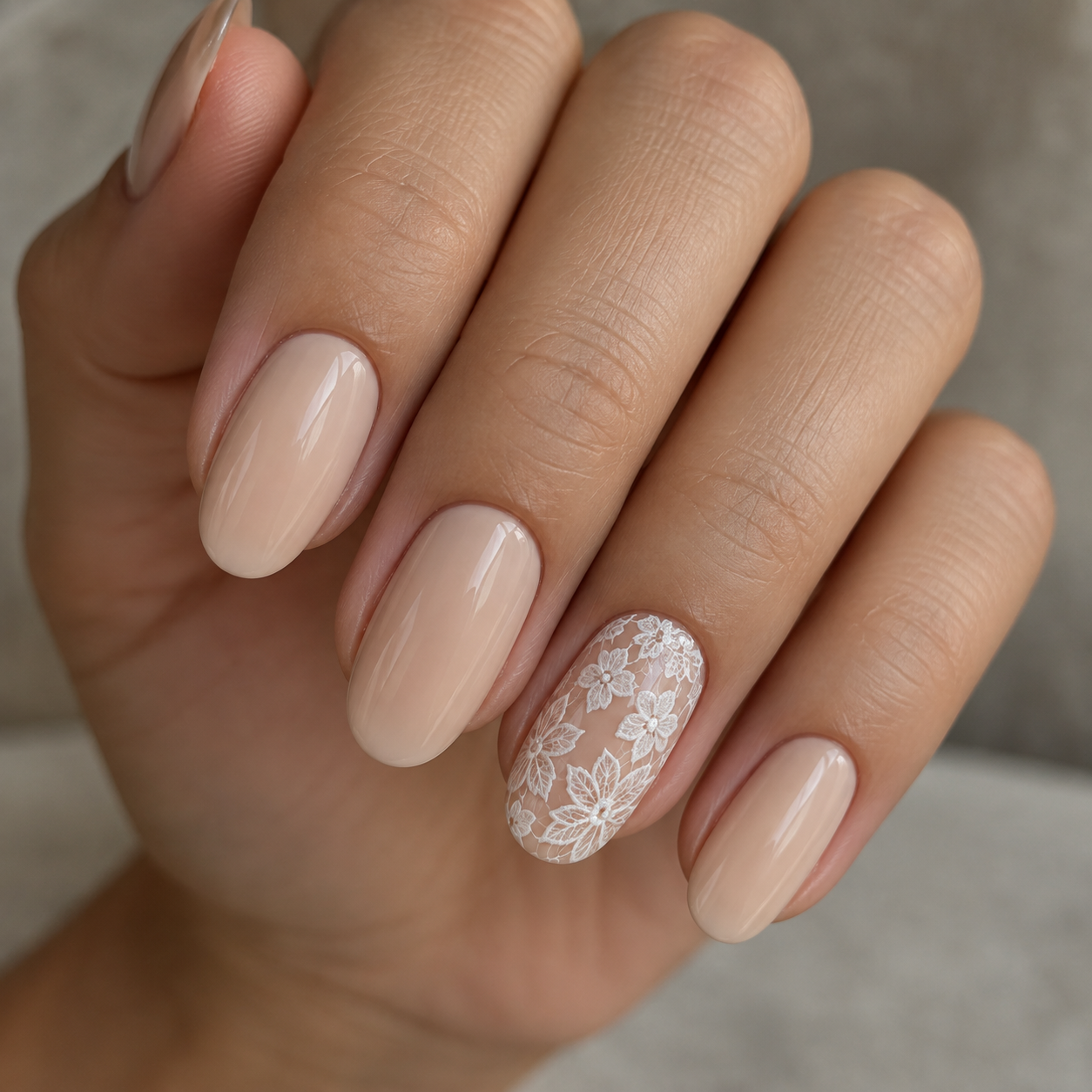 Glossy nude manicure with white floral lace on the ring finger only.