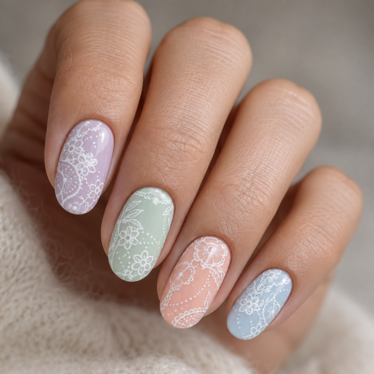 Four nails painted in pastel lavender, mint, peach, and blue, each featuring intricate white lace and floral nail art patterns.