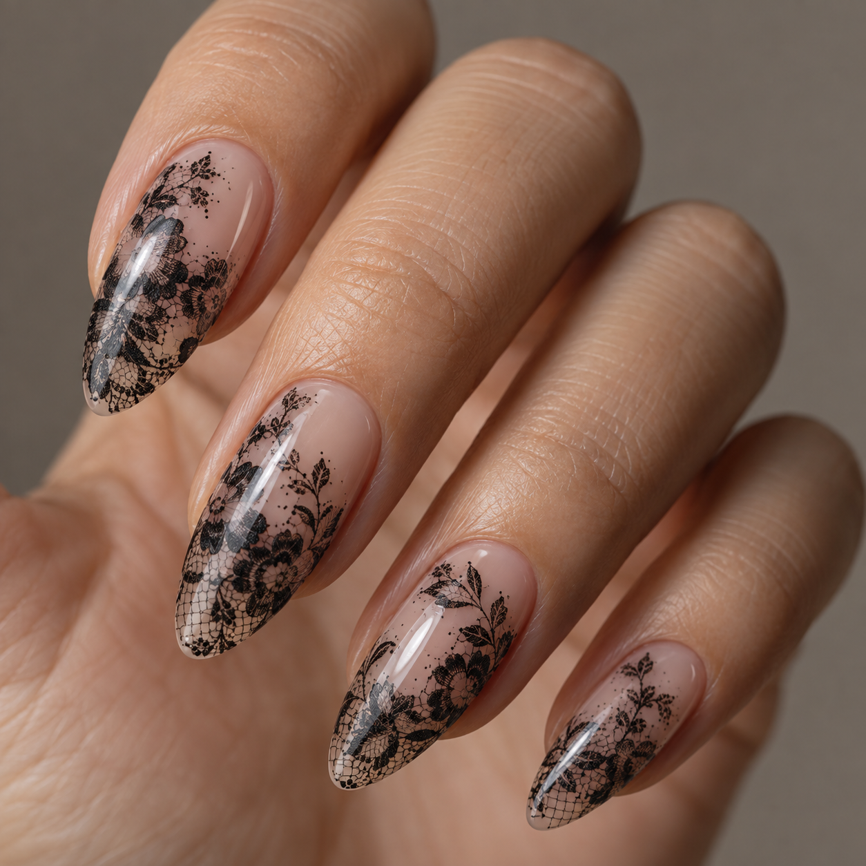 Almond-shaped nails feature a nude base with intricate black lace and floral stamping designs, creating an elegant, high-contrast manicure.