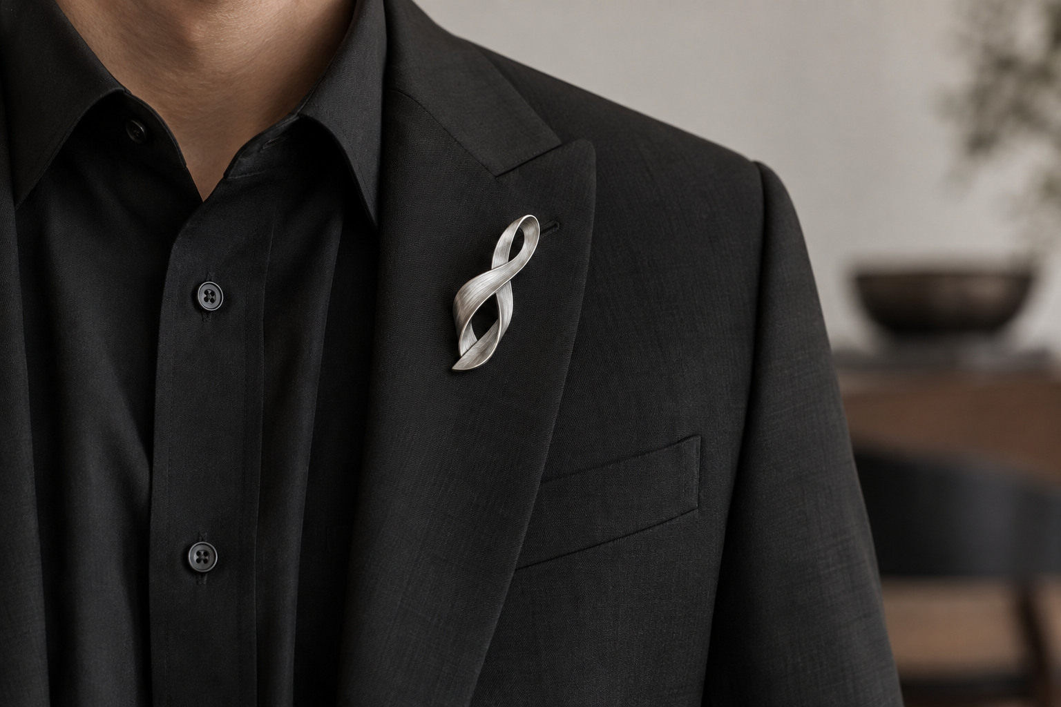 Sculptural silver ribbon brooch on black tailoring.