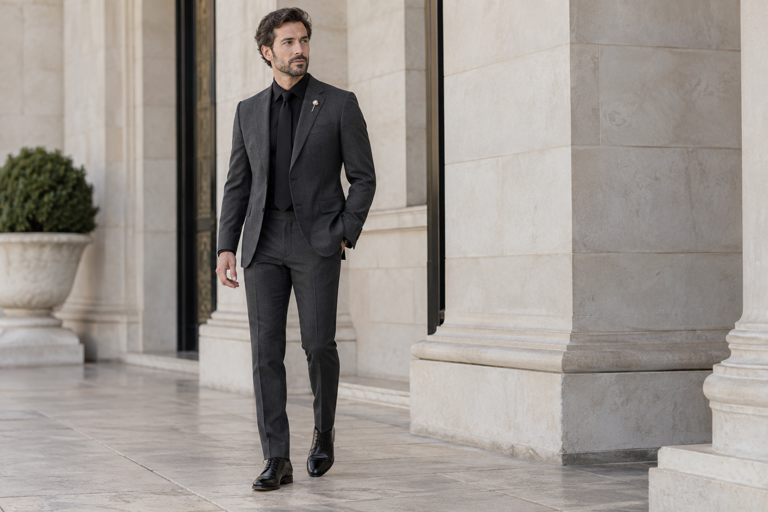 Charcoal suit with black shirt, black shoes and a pearl pin.