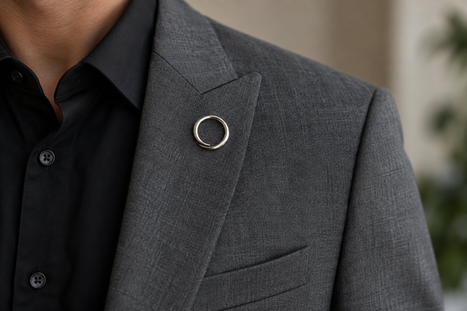 Silver circle brooch on a gray suit with a black shirt.