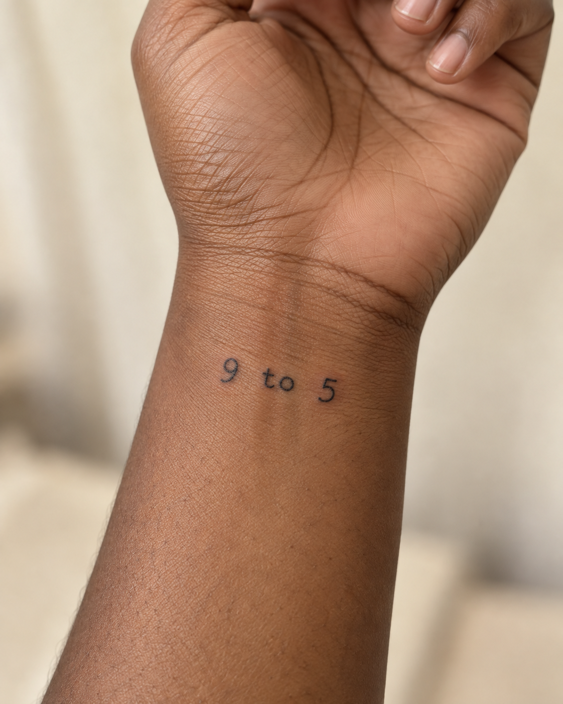 A close-up of a person's inner wrist featuring a small, black ink tattoo that reads "9 to 5" in a simple serif font.