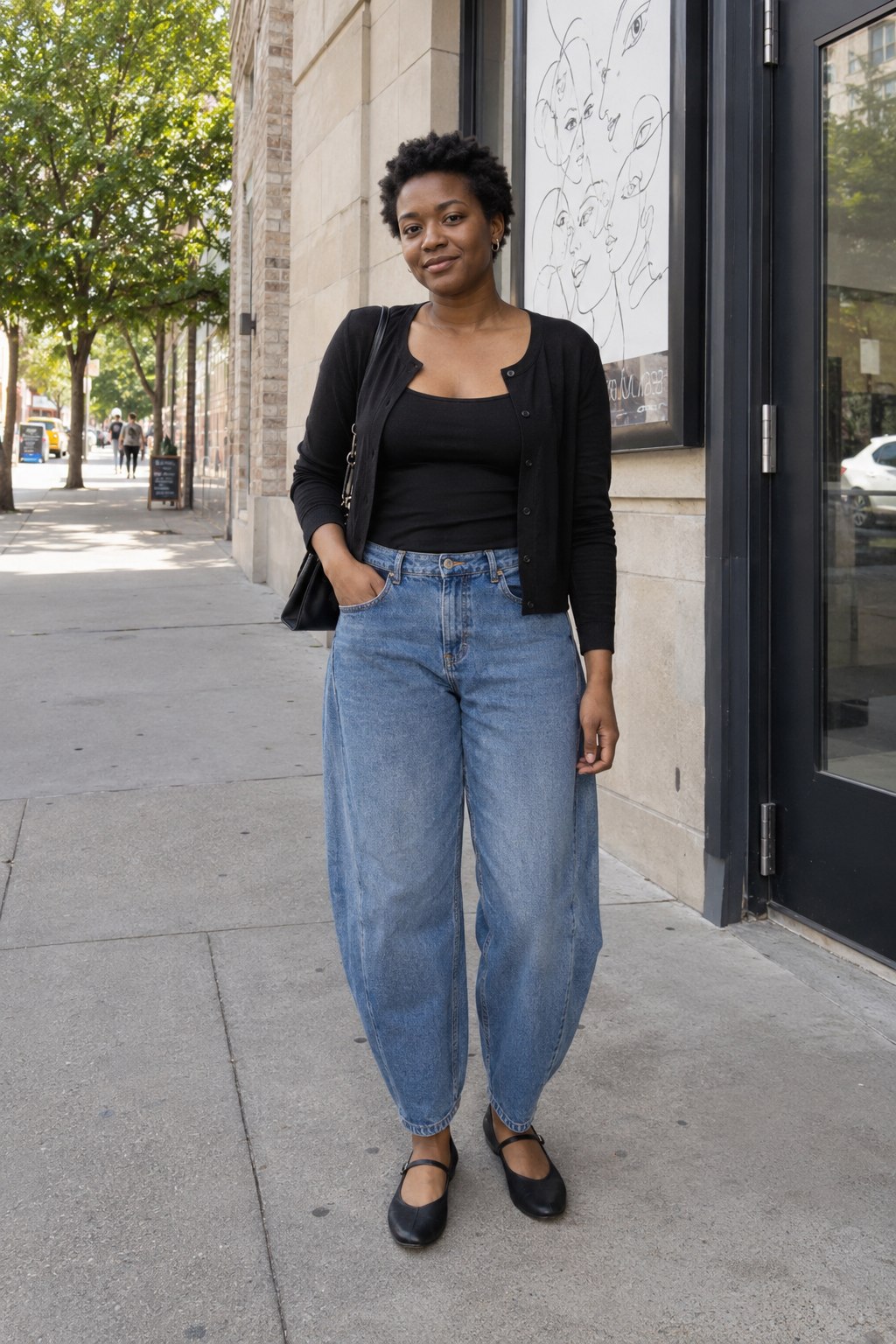 Woman wearing a fine black cardigan, blue barrel jeans and black Mary Jane flats on a paved street.