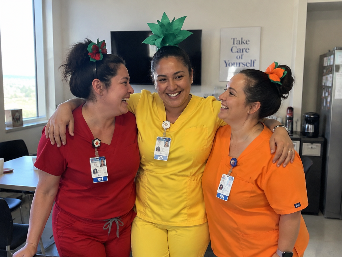 Three healthcare workers in red, yellow and orange scrubs dressed as a strawberry, pineapple and pumpkin