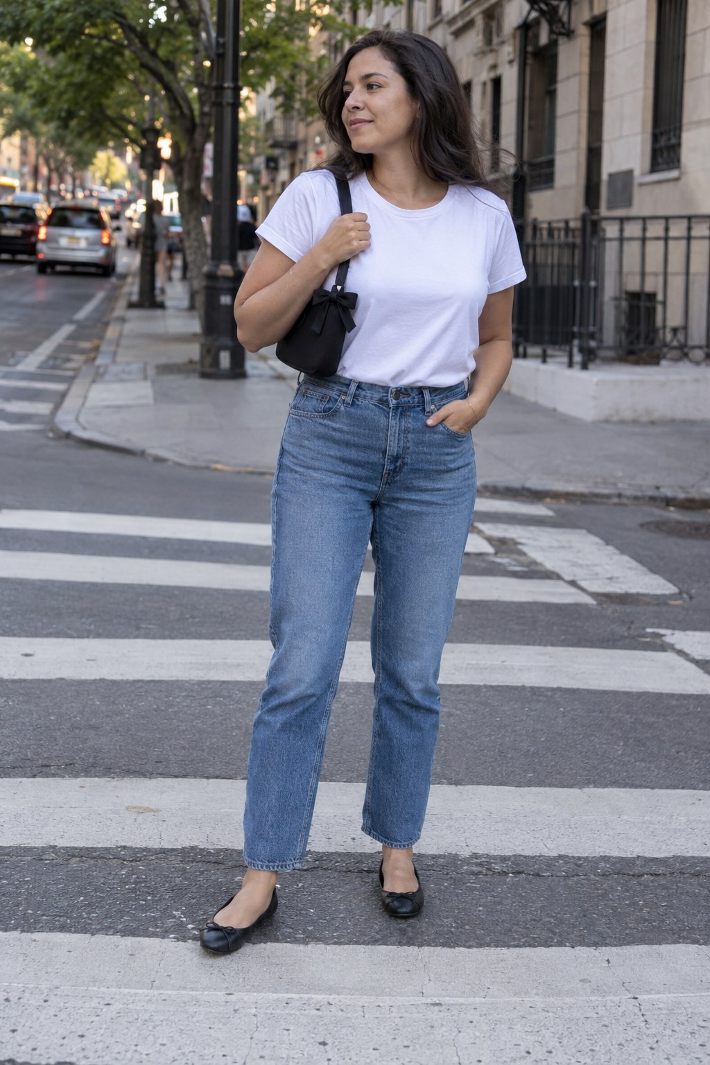 Woman carrying a small black shoulder bag with a subtle bow detail while wearing jeans and a white tee.