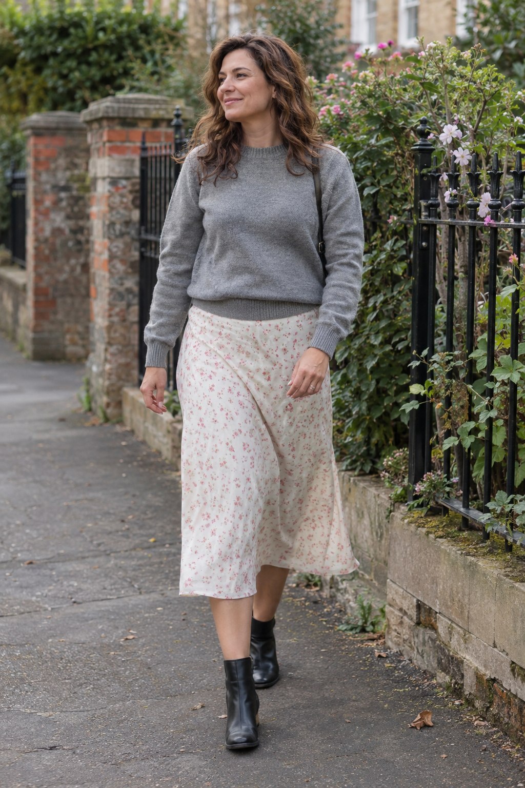 Woman in a small floral-print midi skirt with a plain gray sweater and black ankle boots.