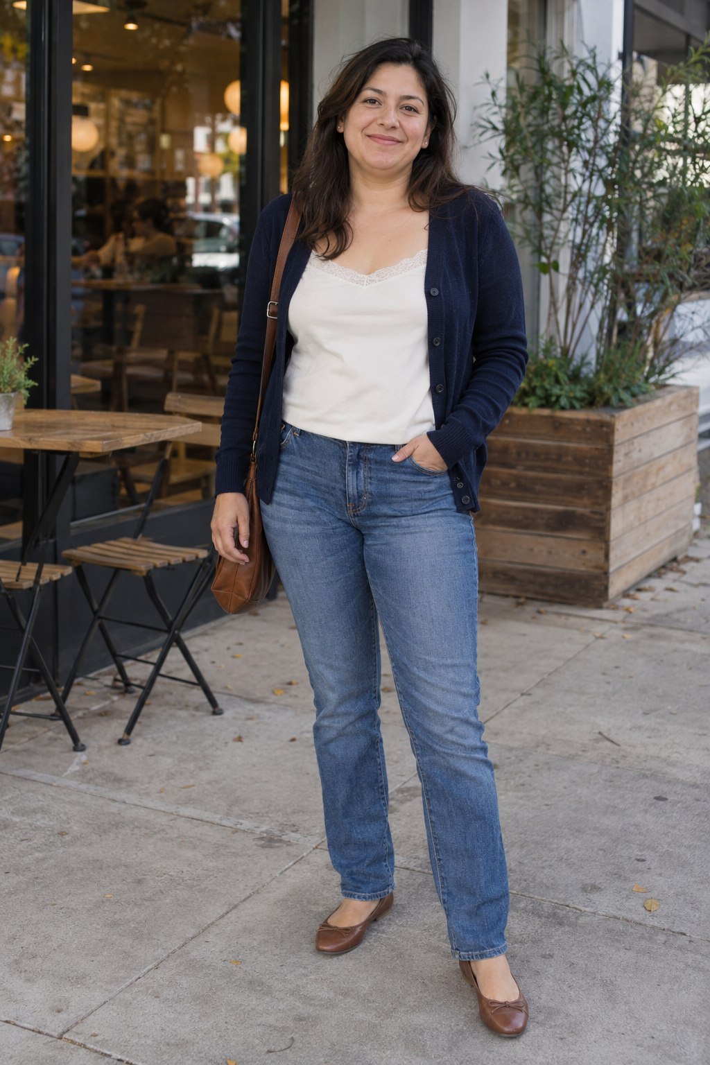 Woman in an ivory lace-trim camisole under an open navy cardigan with straight blue jeans.