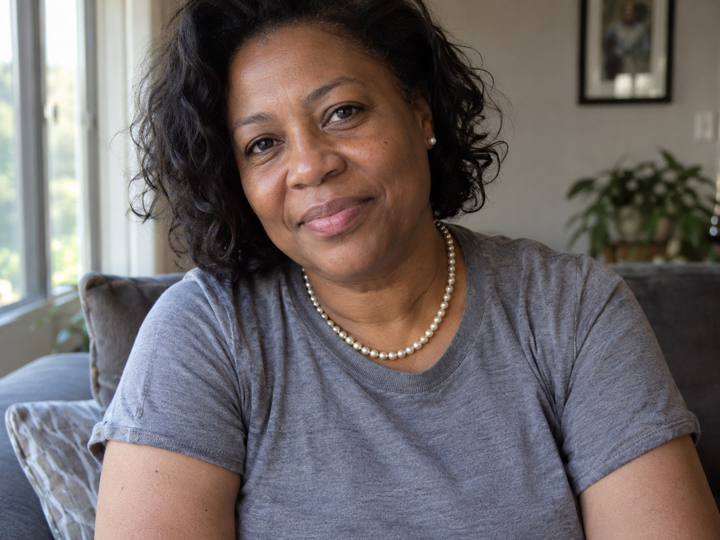 Woman wearing a short cream pearl-style necklace over a plain gray crewneck tee.