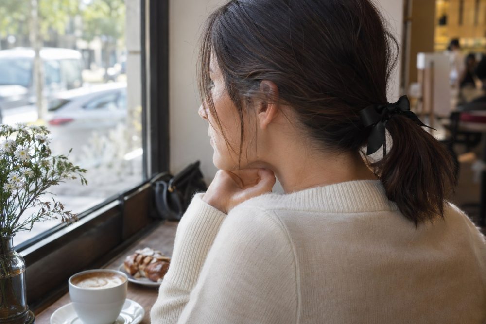 Adult woman wearing a small black ribbon bow in a low ponytail with a cream sweater.