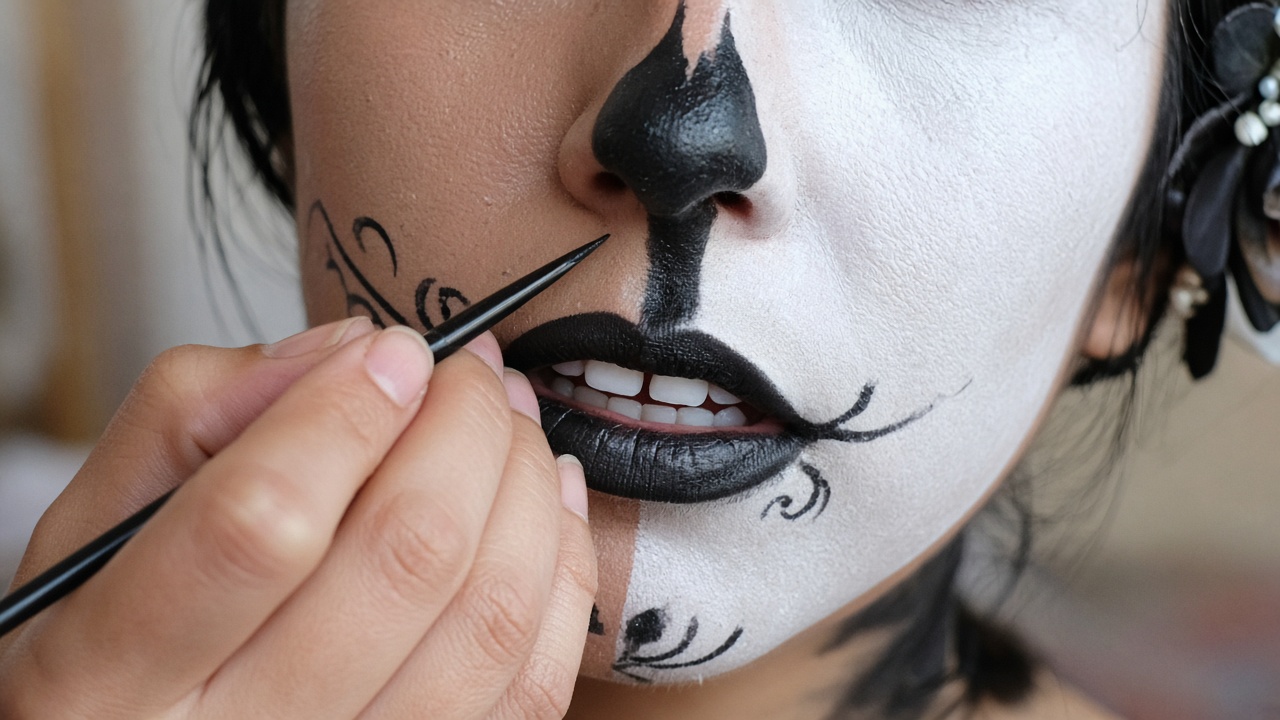 Close-up of hands painting a black nose shape on a white painted face with a fine brush