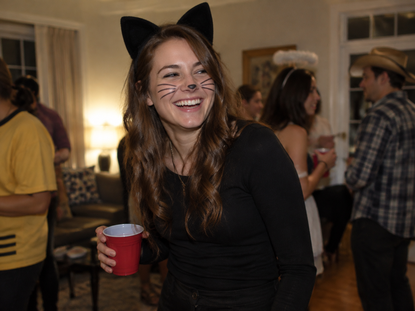 Woman in an all-black outfit with black felt cat ears and drawn whiskers at a party