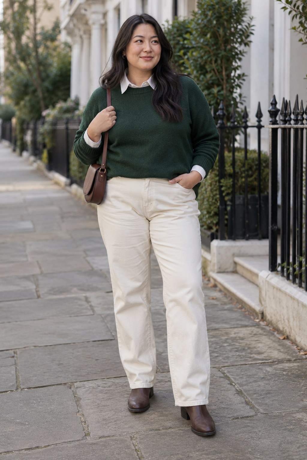 Forest-green sweater and cream jeans with brown Chelsea boots and a saddle bag.