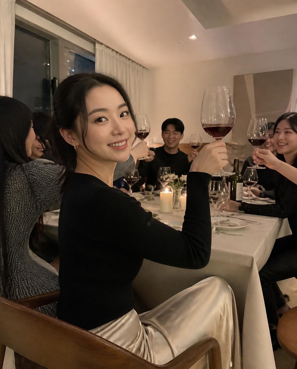 Woman in a champagne satin midi skirt and black fitted knit sweater with gold hoops raising a wine glass for a toast at a candlelit dinner party