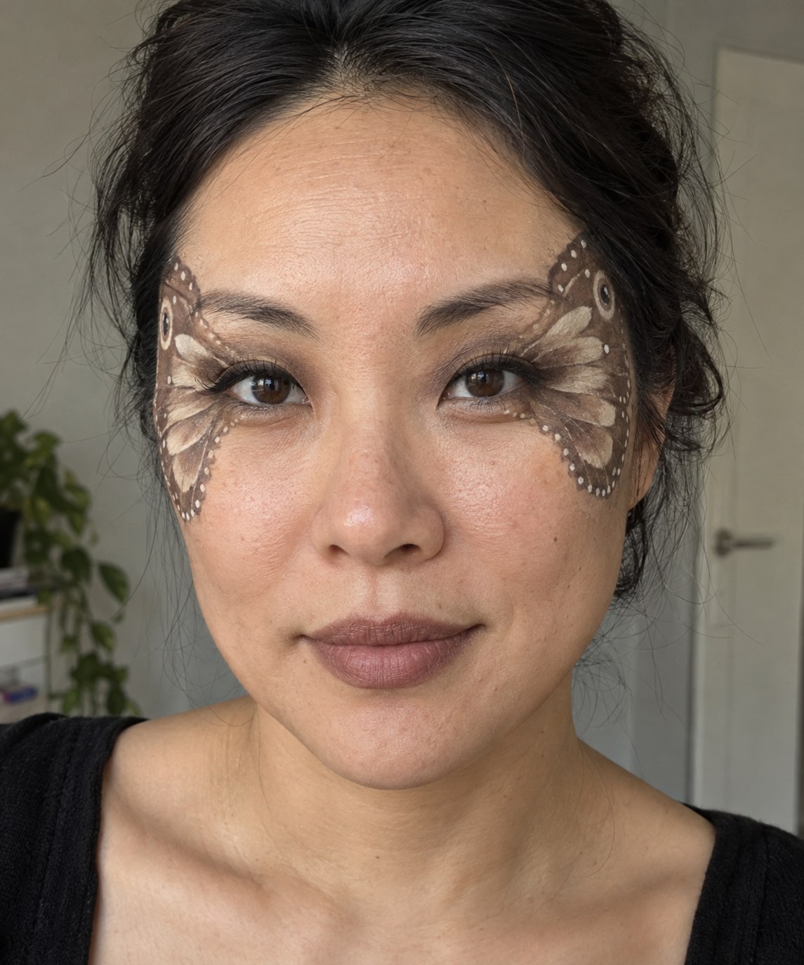 Moth-inspired Halloween makeup with brown and ivory wing shapes extending toward the temples.