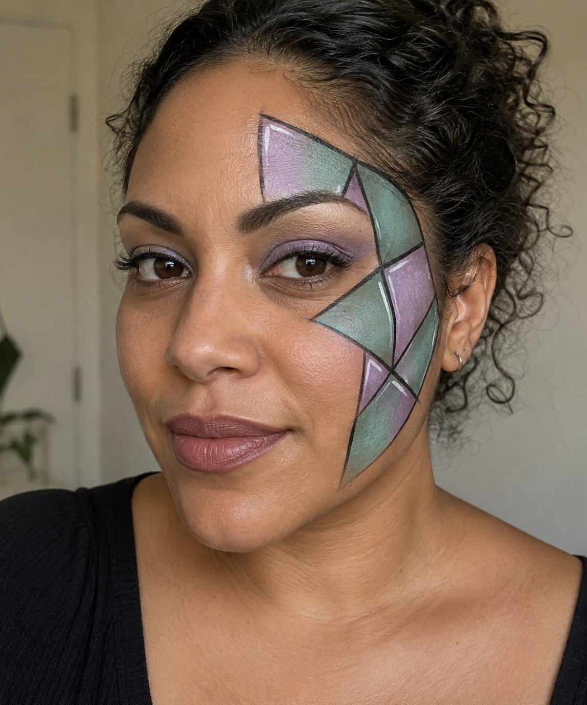 Halloween makeup with lilac and pale teal stained-glass shapes outlined in black across one cheek and temple.