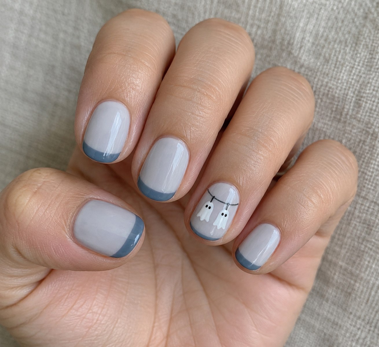 Pale gray manicure with two miniature sheet ghosts hanging from a painted laundry line
