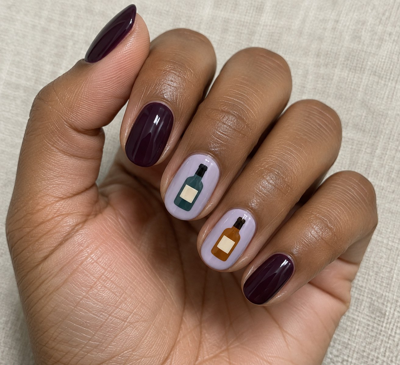 Deep plum nails with small painted potion bottles on two pale lilac accent nails