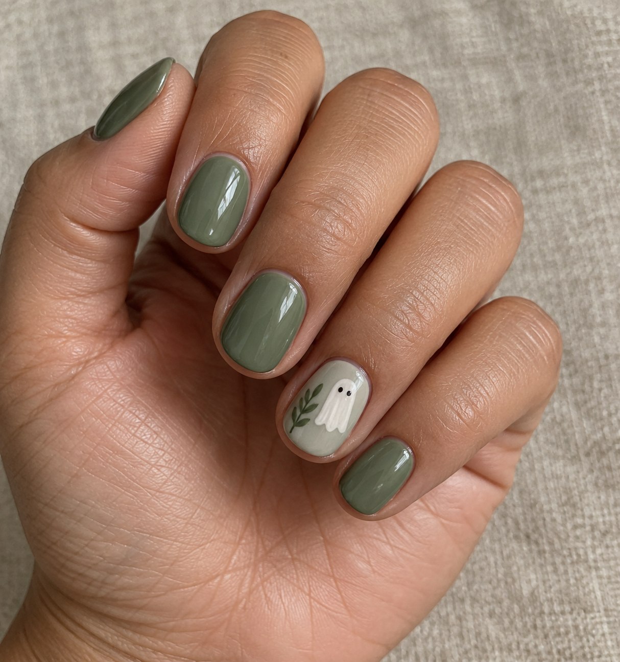 Short sage manicure with one small ghost accent showing a simplified Halloween nail layout