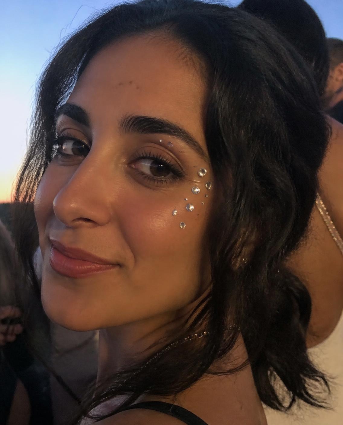 Woman with small rhinestone face gems at the outer corner of her eye, smiling softly
