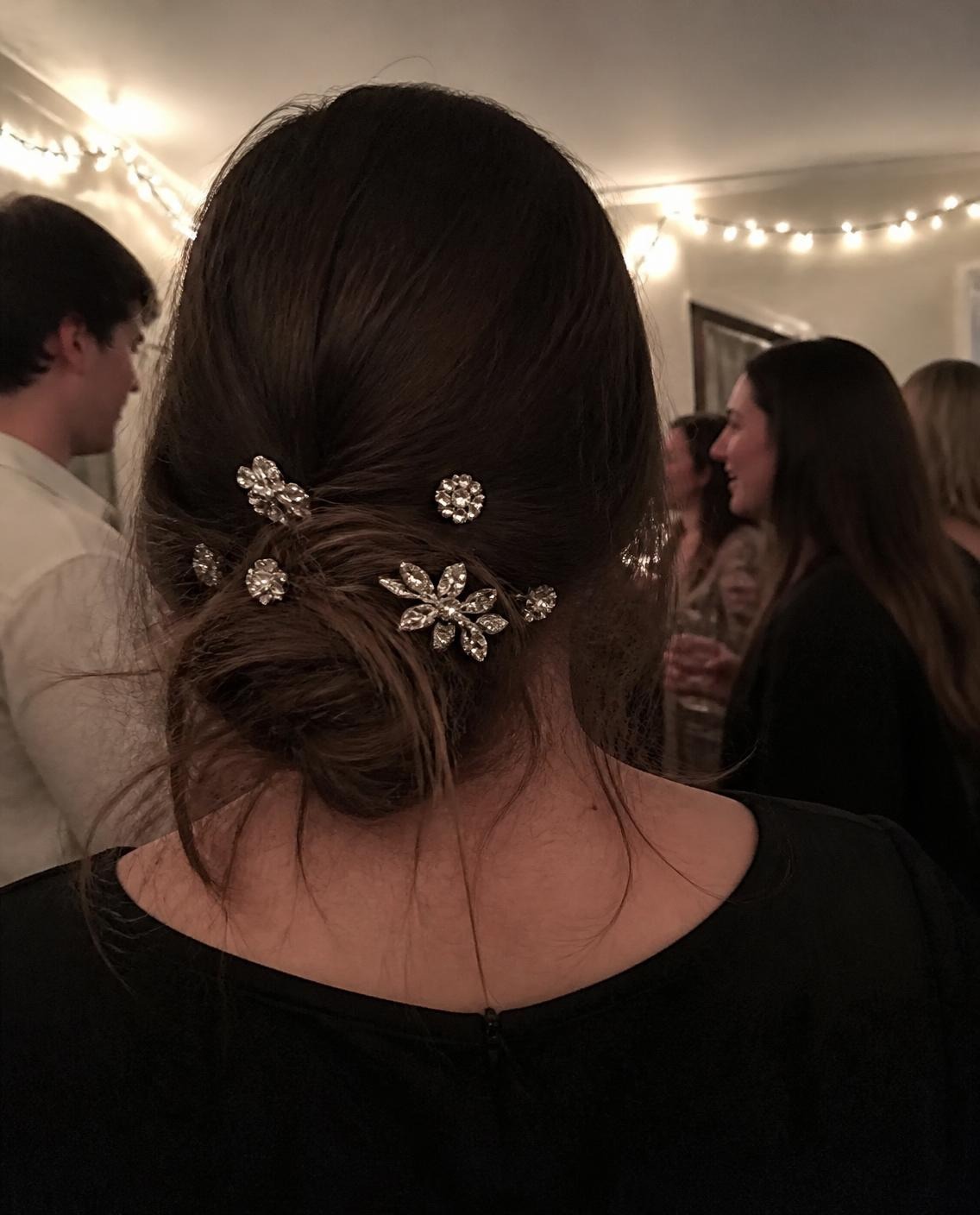 Woman with a low messy bun decorated with sparkly rhinestone flower hair pins at a party lit with fairy lights