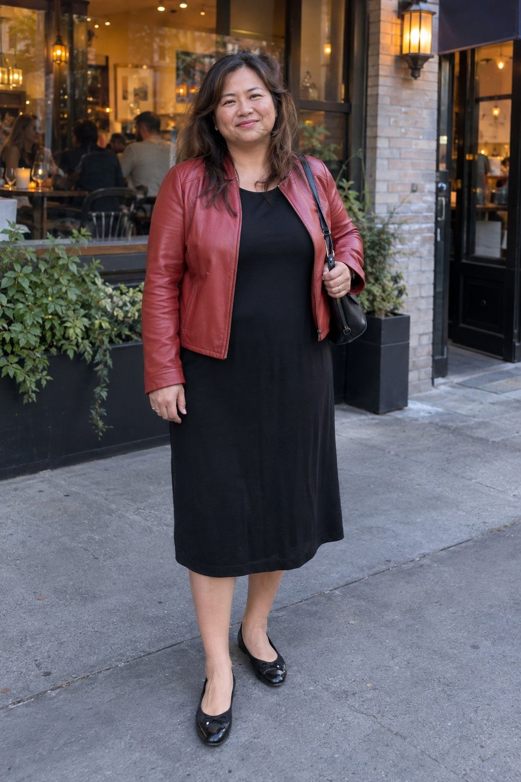 Woman wearing a red leather jacket over a plain black midi dress with black ballet flats.